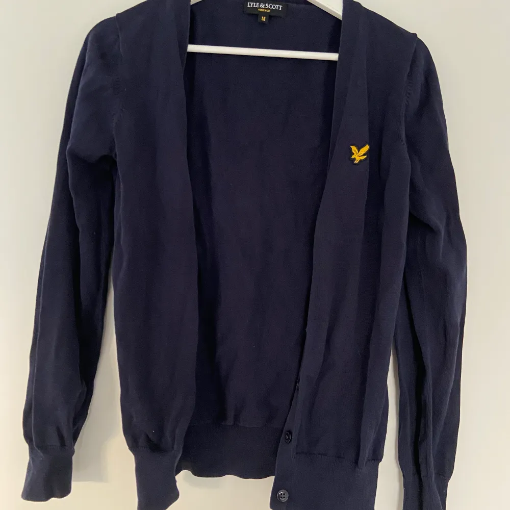 Kofta i mörkt blå, nästan svart färg från Lyle & Scott. Fem knappar, ribbade muddar. Perfekt under vintern!. Stickat.