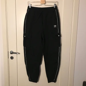 Adidasbyxor - Svarta ”cargopants” från adidas! Köpta på junkyard i storlek 36 (passar även 38)! Jättesköna och dom har även en vit rand längst varje ben som även har reflex-känsla som lyser upp ;)) 🌟 köparen får stå för frakt 😇