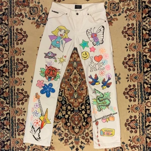 Vita raka y2k Gant custom custommade jeans - As feta raka vita custom Gant jeans med tryck av bla. the iconic Totally Spies och Pokémon 🛍 Det perfekta paret jeans för den som kan rocka ett par super extra byxor med grafisk illustration över hela benen! Så snygga till emot edgy boots och en mörk graphic tee som kontrast eller ett par stora sneakers och en matchande baby tee! W 32, L 34  Alla priser är inkl. frakt och alla plagg tvättas innan de skickas iväg