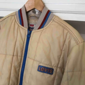  - Väl använd vintage Levis täckjacka. Uppskattningsvis från tidigt 90-tal. En del fläckar samt fläckar av färg på ena armen. Fodret i sömmen bak på ryggen har hål. Trots detta en fräsig jacka. Kan hämtas i Uppsala eller skickas mot fraktkostnad