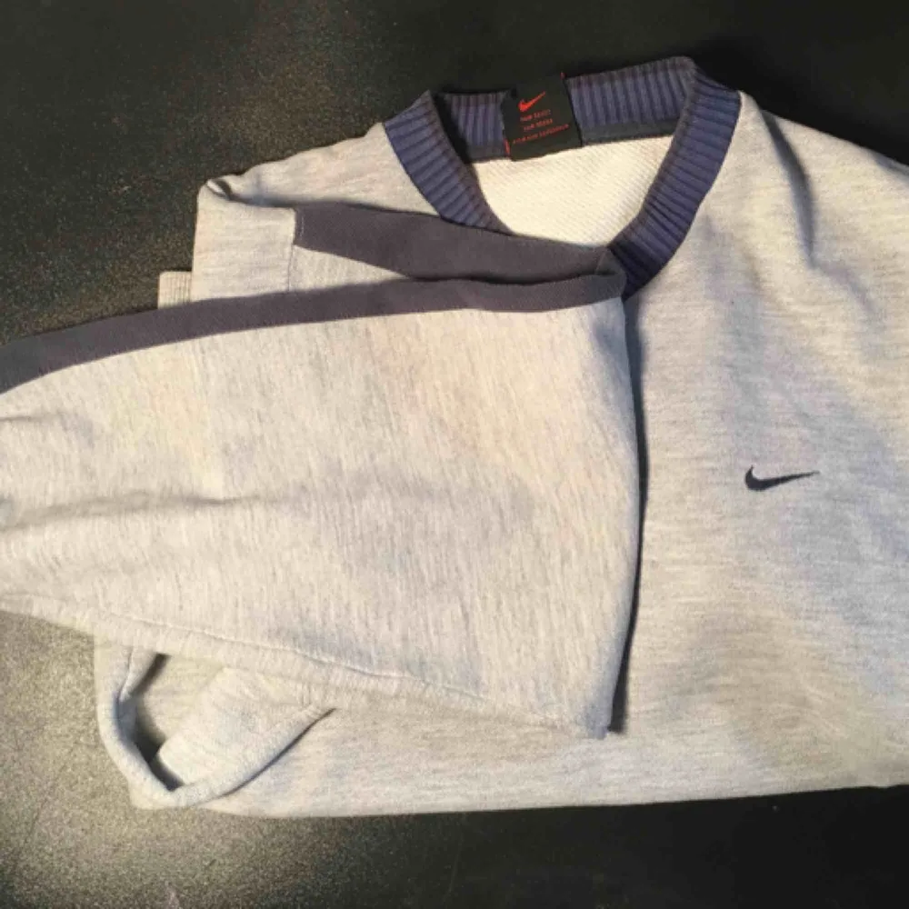 En mysig grå Nike sweater med blå rand på ärmarna och v-hals. OBS! På sista bilden ser man två små vid halsen, men inget man tänker på eller syns tydligt.. Hoodies.
