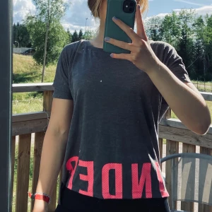 Topp från Under Armour HELT NY - Grå träningstopp från Under Armour med rosa text som fortsätter på baksidan. Stl. XS. Helt ny med tags kvar. Betalning sker via swish. 100kr+frakt!🥰
