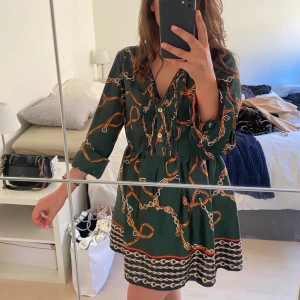 Mönstrad zaraklänning - Grön med kedjemönster över hela och lite puffigare från midjan neråt. Storlek XL men blir perfekt med skärp i midjan. Knäppningen framtill går hela vägen upp som ni ser på bild två men man kan vika in tygdelarna som jag gjort på första bilden, funkar topp