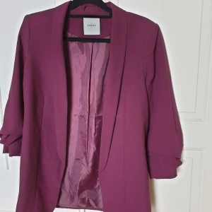 Kavaj, lila/vinröd - Kavaj från zalando, storlek M. Köpt till ett specifikt event och bara använt en gång. Smoking stil på kavajen, ¾ ärm (se bild 3), inga fickor eller knappar men superbekväm och snygg. Säljer den för att den är lite för tajt över mina breda axlar.