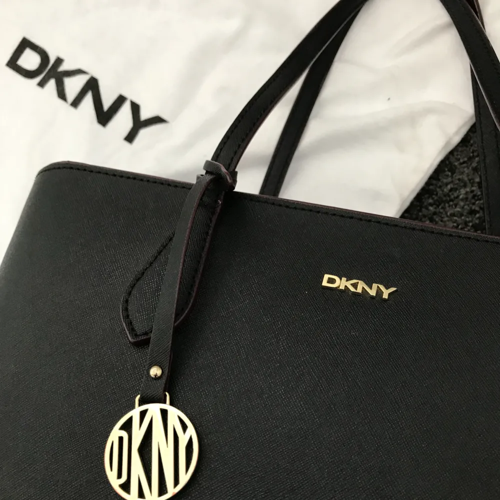Äkta DKNY väska köpt i USA. Snygg svart väska med guldiga och vinröda detaljer. Dustbag kommer med. Mycket fint. Möts upp i Stockholm och fraktar (köparen står för frakten). Väskor.