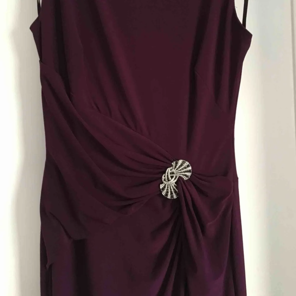 Mycket fin lila långklänning från Ralph Lauren, endast använd en gång. Vacker dekorativt smycke på klänningen och slits nertill. Passar storlek 36/38.   Ord.pris 2295 kr säljs nu för 1300 kr. Klänningar.