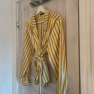  - Jättefin blus i sidenmaterial, vit och gul! Har knappar längst ut på armen och bälte i midjan!  Du som kund står för frakten