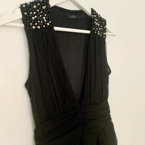 Ny klänning/ Storlek S/ Från Jeane Blush - Helt ny festklänning från märket Jeane Blush, som tyvärr inte kommit till användning. Klänningens axlar pryds av vita och svarta pärlor. Klänningen stängs med en diskret dragkedja på sidan i midjan. Klänningen har en rätt djup v-ringning. Storlek S. 