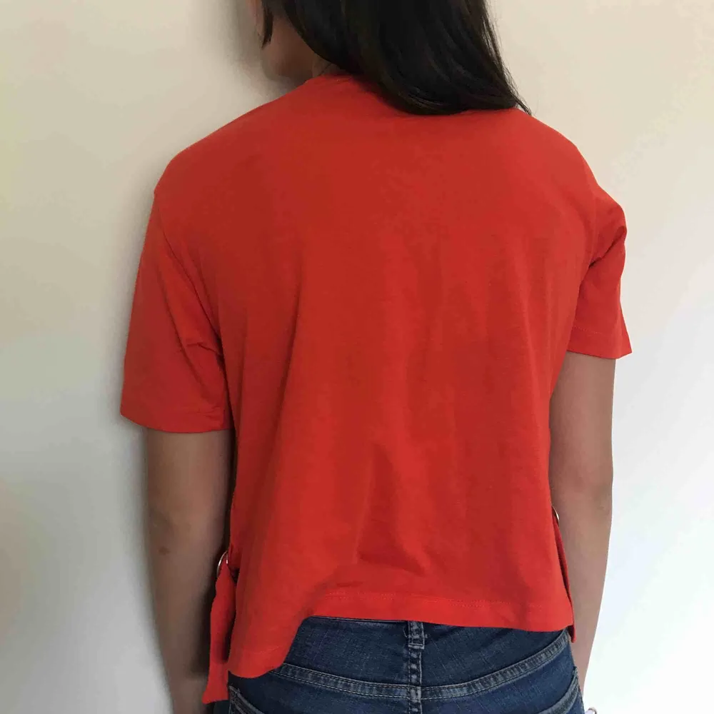 En röd t-shirt med detaljer på sidorna med band och metall. Kostar 150kr inklusive frakt.. T-shirts.
