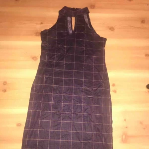  - Sexig klänning som räcker en bit över knäna med halterneck och rutigt mönster. Passar en med kurvor! Lila med mörkgula detaljer. Knappar bakom nacken. 