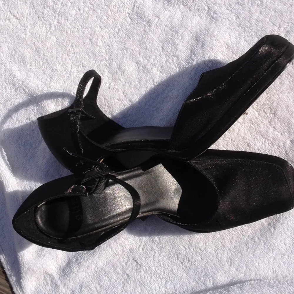 Svarta glittriga högklackade skor med fyrkantig tå och smal 10 cm hög klack. 
Smalt spänne vid vristen. Märke Elle. Tillverkade i Vietnam. Inköpta år 2000. Fint skick, knappt använda. Perfekt till festklänningen! . Accessoarer.