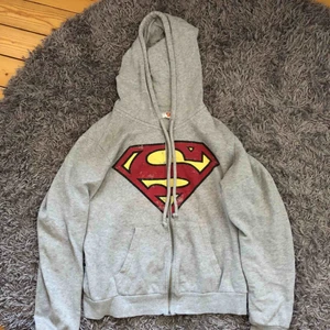 - En grå luvtröja med dragkedja, superman tryck.  Bra skick, märket ska se slitet ut.  Köpare står för frakt. 