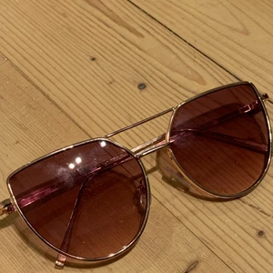 Solglasögon  - Oanvända solglasögon i en brunaktig ton. Ramen är guldig. 