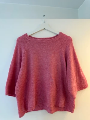 Rosa stickad tröja från 157 - Mysig rosa stickad tröja från 157 med trekvartsärm. Tröjan har en loose passform och ribbade kanter vid ärmslut och nederkant. 