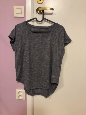 Grå tränings-tshirt från SOC XS - Mörkgrå melerad tränings-tshirt från SOC i storlek XS. T-shirten har rund halsringning och korta ärmar, tillverkad i ett lätt och snabbtorkande funktionsmaterial som andas. Perfekt för gymmet eller löprundan.