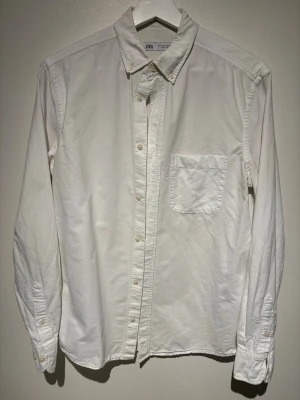 Vit skjorta från Zara S - Klassisk vit skjorta från Zara med lång ärm, bröstficka och knappar framtill. Skjortan har en stilren design och är tillverkad i bomull, perfekt för en clean och enkel look.