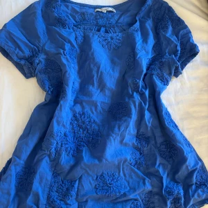 Blå blus med broderade blommor - Säljer en fin blå blus med broderade blommor över hela plagget. Köptes i Grekland💙använd 1 gång