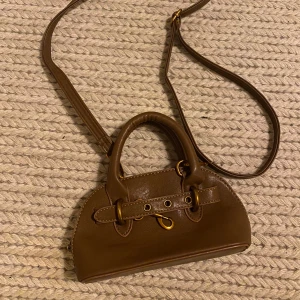 Brun väska  - Brun väska med gulddetaljer, justerbart band. 