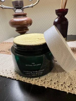 The Ritual of Jing body cream - Oöppnad. Lyxig body cream från Rituals i serien The Ritual of Jing. Kommer i en mörkgrön burk med guldfärgat lock och vit ytterhylsa. Innehåller doft av lotus och jujube. Perfekt för dig som vill ha en återfuktande och väldoftande kroppskräm.