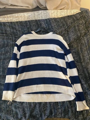 Randig stickad tröja från Canda - Säljer en oversized stickad tröja från Canda med breda marinblå och vita ränder. Tröjan har rund halsringning, lång ärm och ribbade muddar. Perfekt för dig som gillar en chill och avslappnad stil. ( jag fattar inte riktigt varför det står tolv men skulle säga att det är typ en 36)