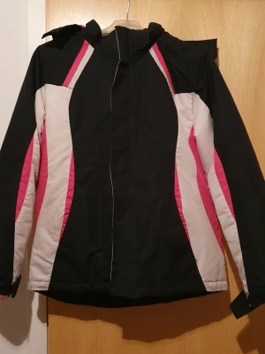 Vinterjacka - Snygg vinterjacka från George i svart, rosa och vitt. Jackan har huva med mjukt rosa fleecefoder, dragkedja framtill och coola färgblock längs sidorna. Perfekt för kalla dagar och riktigt skön att bära. Passar dig som vill ha en sportig look. Det är i storlek M i barnstorlek. Har några fläckar.