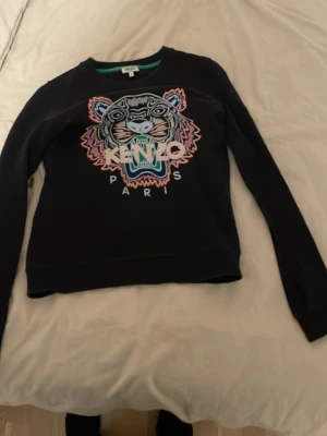 Svart Kenzo sweatshirt med tiger - Cool svart sweatshirt från Kenzo med ikoniskt broderat tigerhuvud och färgglada detaljer framtill. Tröjan har rund halsringning och långa ärmar. Perfekt statement-plagg för dig som vill sticka ut.