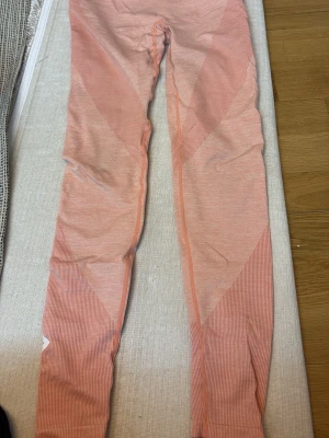 Rosa leggings med mönster - Säljer ett par snygga rosa leggings med diskret randigt mönster och geometriska detaljer. De är stretchiga och sitter tight, perfekta för träning eller chill. Materialet känns mjukt och följsamt mot huden.