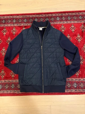 Mörkblå cardigan jacka från BOSS - Stilren mörkblå cardigan jacka från BOSS med dragkedja framtill och ribbade muddar. Jackan har släta ärmar, hög krage och två fickor. Den passar till alla lägen, allt från festliga tillfällen och casual lägen. Jackan passar storleken S och är perfekt till kommande vår och sommarkvällar. Priset är ej hugget i sten och kom gärna med frågor.