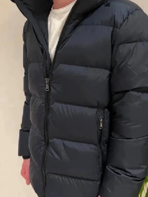 J.Lindeberg jacka  - Säljer en navy blå pufferjacka från J.Lindeberg med huva och två sidofickor med dragkedja. Jackan har ett stilrent emblem på vänster ärm och grova, horisontella sömmar som ger en schysst look. Perfekt för kalla dagar och enkel att matcha med jeans