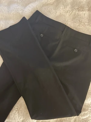 Svarta kostymbyxor från Esprit - Snygga svarta kostymbyxor från Esprit med raka ben och klassiska passpoalfickor bak med knapp. Byxorna har bälteshällor och stängs med dragkedja och hake. Perfekta till en stilren look och passar till skjorta eller t-shirt.