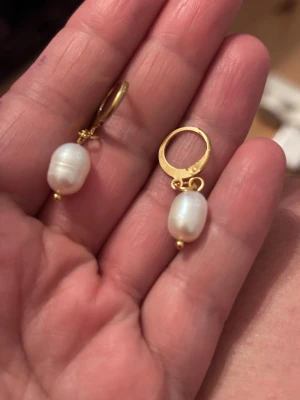 Guldörhängen med vita pärlor - Säljer ett par stilrena örhängen i stål  ringar med  droppformade söttvattenspärlor . Klassisk design som ger en elegant touch till din look. Perfekta för dig som gillar tidlösa accessoarer.