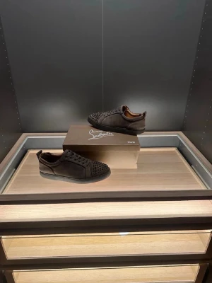 Gråa Christian Louboutin sneakers - Säljer ett par gråa sneakers från Christian Louboutin i mocka med ikoniska röda sulor. Skorna har snörning och coola nitar på tån för extra edge. Perfekta för dig som vill sticka ut med exklusiv design och lyxiga material. 🙌 Pris ej hugget i sten 🪨.