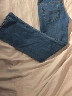 Levi's 501 blå jeans 140 cm - Klassiska blå Levi's 501 jeans med rak passform och femficksmodell. Tillverkade i bomull med snygga kontrastsömmar och ikonisk bakficka. Perfekta för dig som gillar tidlös denimstil.