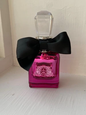 Juicy Couture parfym rosa flaska - Snygg parfym från Juicy Couture i en rosa flaska med svart rosett. Doftens huvudnoter är fruktig, vit blomma, träig, karamell, vanilj, söt, citrus, pudrig och amber. Perfekt för dig som gillar lekfulla och trendiga dofter. Full flaska och endast testad, 50ml. 🩷
