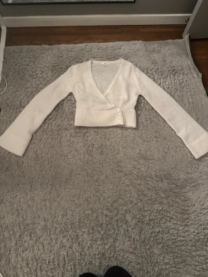 Ljusvit omlottkofta från Gina Tricot storlek 158/164 - Supersöt ljusvit omlottkofta från Gina Tricot med v-ringning. Koftan har långa ärmar, knytband på insidan och fyra små knappar framtill. Perfekt att slänga över ett linne! Super finnn❤️