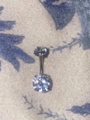 Navelpicrcing - Bilderna visar ett smycke, troligen en navelpiercing med två glittrande stenar, men ingen väst syns.