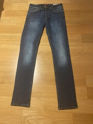 Jack & Jones Slim Glenn jeans blå 28/32 - Snygga blå jeans från Jack & Jones, modell Slim Glenn. De har en slim passform med raka ben och klassisk femficksdesign. Jeansen är tillverkade i bomull med lite stretch för extra komfort. Färgen är mörkblå med snygga slitningar och kontrastsömmar.