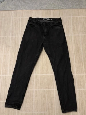 Svarta jeans från Indicode - Säljer ett par svarta jeans från Indicode i storlek 30/32. Jeansen har klassisk femficksdesign, rak passform och normal midja. Färgen är mörk svart med lätt tvättad look. Jensen har blivit använda ett flertal gånger men är i ett helt okej skick. Killen i bilden är 172 cm lång för referens.