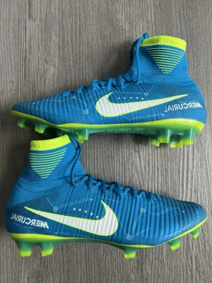 Nike Mercurial Neymar fotbollsskor blå - Säljer ett par Nike Mercurial Neymar fotbollsskor i blått med vita och neongula detaljer. Skorna har hög strumpkrage, snörning och mönstrad ovandel i syntet och flyknit. Sulan är neongul med dobbar för gräsplan. Perfekta för dig som vill sticka ut på planen.