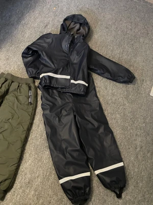 Svarta täckbyxor med reflexdetaljer - Mörkblå täckbyxor med reflexband vid bensluten och justerbara fothällor. Insidan är fodrad med mjuk fleece för extra värme. Byxorna har resår i midjan och bensluten för att sitta på plats. Perfekta för kalla och blöta dagar.