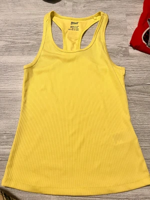 Gul ribbad linnetopp  - Säljer en fräsch gul linnetopp i storlek M. Toppen är ribbad och har en sportig racerback-design som ger en snygg och bekväm passform. Perfekt för träning eller somrig stil. Materialet är mjukt och stretchigt för extra komfort.