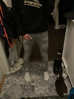 Grå skinny jeans från Dsquared2 - Säljer ett par grå jeans från Dsquared2 med skinny passform och låg midja. Jeansen har coola vita färgstänk och klassisk femficksdesign. Materialet är jeans och de har knapp och dragkedja framtill. Märkeslapp bak och Dsquared2-tag vid gylfen.