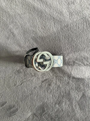 Gucci bälte  - Gucci GG Supreme bälte med klassiskt monogrammönster i beige och blått. Bältet har en stor, rund silverspänne med GG-logga och insida i ljust brunt skinn. Perfekt accessoar för att lyfta vilken outfit som helst.