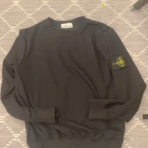 Svart sweatshirt från Stone Island - Svart långärmad sweatshirt från Stone Island med klassisk rund hals och ikonisk logotyp-patch på ärmen. Tröjan är tillverkad i mjuk bomull och har ribbade muddar vid ärmslut och nederkant. Perfekt för dig som gillar streetwear och snygga detaljer.