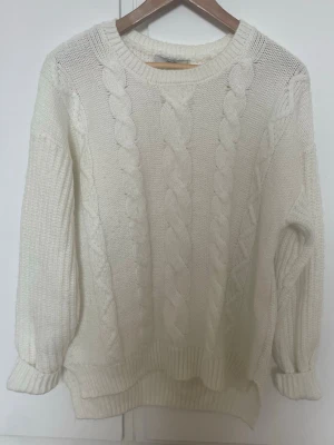 Vit stickad tröja från George - Står inte storleken på men jag gissar på M. Mysig vit stickad tröja från George med grova flätstickade detaljer på framsidan och ribbade muddar. Tröjan har rund hals och långärmade ärmar, perfekt för kyliga dagar. Materialet är mjukt och tjockt, vilket gör den extra skön att bära.
