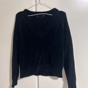 Svart stickad tröja med v-ringning - Mysig svart stickad tröja med bred v-ringning och ribbade detaljer vid hals, ärmslut och nederkant. Tröjan har lång ärm och är tillverkad i ett mjukt material som känns skönt mot huden. 