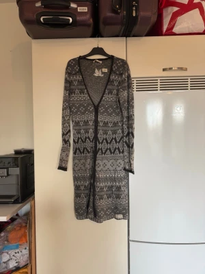 Mönstrad lång kofta Odd Molly - Säljer en svart, grå och vit lång kofta från Odd Molly med snyggt geometriskt mönster. Koftan har v-ringning, långa ärmar och knyt framtill. Materialet är mjukt och stickat, perfekt för lager-på-lager under höst och vinter. Passar dig som gillar unik design och detaljer. SAMPLE. Storlek 1 som enligt deras storleksguide motsvarar en storlek S. Mycket fint skick, jag hittar inga synliga anmärkningar eller defekter. 