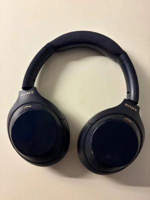 Sony WH-1000XM4 hörlurar - Sony WH-1000XM4 trådlösa over-ear hörlurar med aktiv brusreducering. Mörkblå färg, litet litet slitage på kåpor och inuti öronkuddarna (har rengjort så gott det går) men i väl fungerande skick. Perfekt för musik och samtal med lång batteritid och bekväm passform.