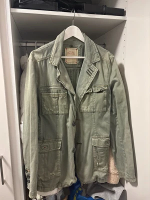 Grön jacka från Jack & Jones - Säljer en grön jacka från Jack & Jones Vintage Denim med flera fickor, knappstängning och coola detaljer som broderade sömmar och tryck baktill. Jackan har klassisk krage och lång ärm, perfekt för dig som gillar street och utility vibes.