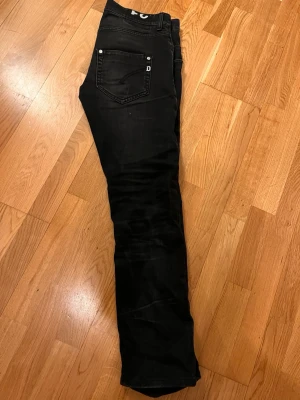 Svarta Replay Anbass jeans herr - Säljer ett par svarta dondup jeans med klassisk smal passform. Jeansen har silverfärgade nitar och knapp, samt diskret dondup-logga på bakfickan. Materialet är stretchigt jeans för extra komfort och snygg look.